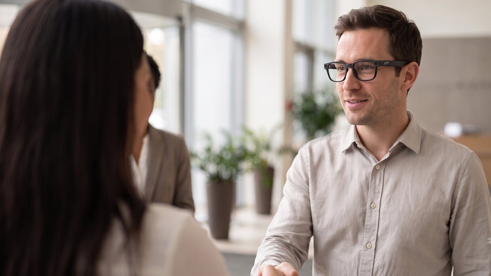 A man wearing AURVIZ o1 smartglasses shakes hands with someone he is being introduced to in an office lobby.